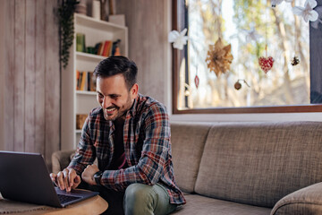 Happy man, using a laptop, working from his house.
