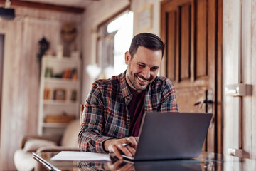 Smiling man working online, typing something on the laptop keyboard.