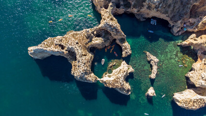 Amazing scenic drone aerial view of the beach and ocean with calm waves during a sunset with vibrant colors. Algarve, Portugal. Clear waters. Holidays and Vacations. Background. Beach with rocks.
