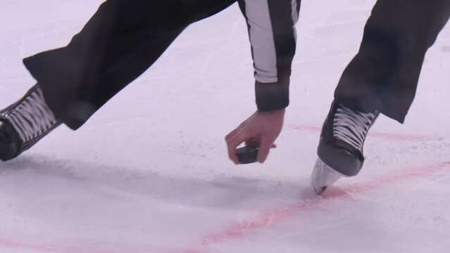 Worker cleans ice rink surface with shovel and referee takes away puck at break in hockey match closeup slow motion