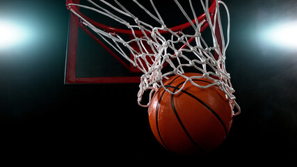 Fototapeta na wymiar Basketball going through the basket on black backgorund