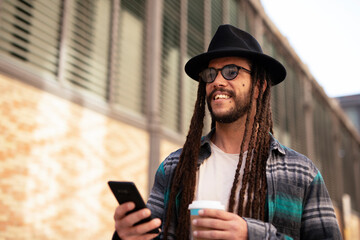 Handsome guy drinking coffee while walking in the street. Modern fashion man using the phone..