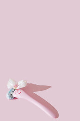 Fototapeta na wymiar A pink women's razor shaving with white petals creative flat lay. Beauty hygiene routine. Body positivity movement and gender inclusiveness idea. Pink background. Sensitive skin idea. Copy space