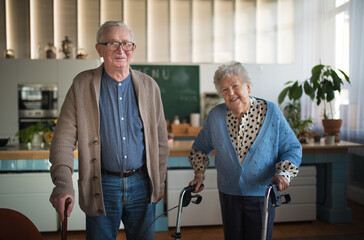 Senior man and woman walking with walker indoors in retirement nursing hme.