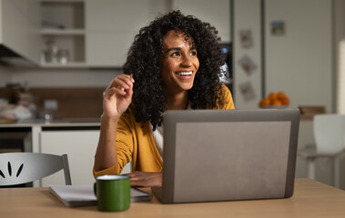 Cinematic shot of pensive smiling brazilian business woman is thinking how to solve problem in best way while doing  smart working with laptop from home in kitchen during covid-19 pandemic lockdown.