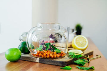 Beautiful glass teapot with sea buckthorn berries, dried thyme and green mint leaves.