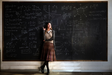 Cinematic shot of young female teacher or student indicates with forefinger at blackboard with math...