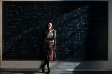 Cinematic shot of young pensive thoughtful female teacher or student leaning against blackboard...