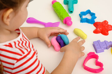 children's hands with multicolored plasticine, play dough on white table
