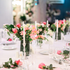 Candles and vase with white roses placed on round table near wineglasses during romantic date in garden