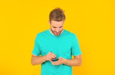 man in blue shirt use stylus and cellphone on yellow background, technology