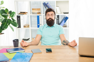 Calm guy meditate keeping mudra listening to relaxing music in headphones at office desk, meditation