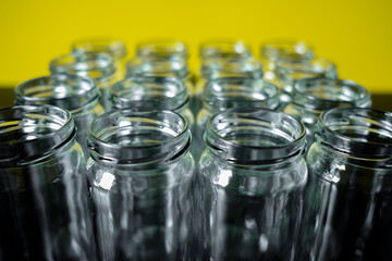 Frontal shot of empty glass jars lined up in a row on a yellow background.