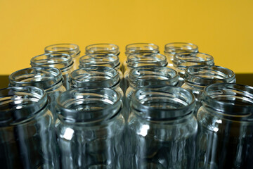Frontal shot of empty glass jars lined up in a row on a yellow background.