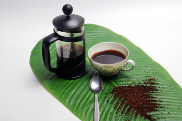 french press coffee with cup of coffee spoon and coarse coffee powder on banana leaf white...