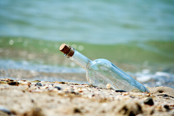 A bottle with a letter thrown out of the sea on a sandy shore.