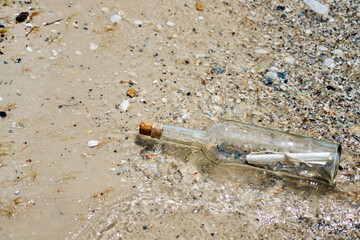 A bottle with a letter thrown out of the sea on a sandy shore.