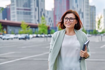Smiling successful mature business woman walking outdoor, modern urban style background.