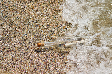 A bottle with a letter thrown out of the sea on a sandy shore.