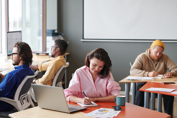 Group of young multi-ethnic self-employed people sitting at tables and working with devices abd papers in coworking space