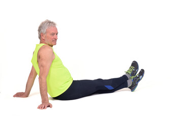 side view of a senior man with sportswear stiitng on the floor looking away on white background