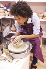 Creative afro-american young woman shaping clay on pottery wheel. Workshop in ceramic studio. Female artist. 
