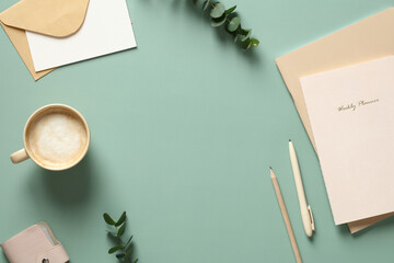 Elegant feminine workspace with cup of coffee, notebooks, eucalyptus leaves on green table. Flat lay, top view.