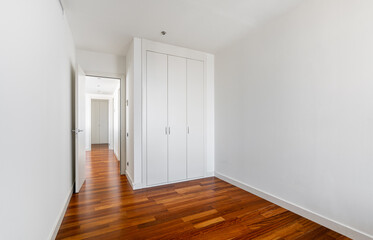 Interior of empty apartment, white room with built-in wardrobe, parquet floor and view to the hallway