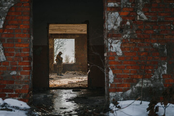 Ukrainian soldier inspect or view destroyed ruined burnt house after shootout . Silhouette of a soldier standing in the middle of a house in the corridor in one of the rooms opposite the window.