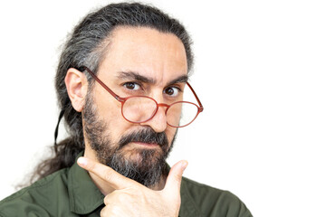 Bearded man with long hair looking over glasses, selective focus. Man pretended to take his hand to his chin.