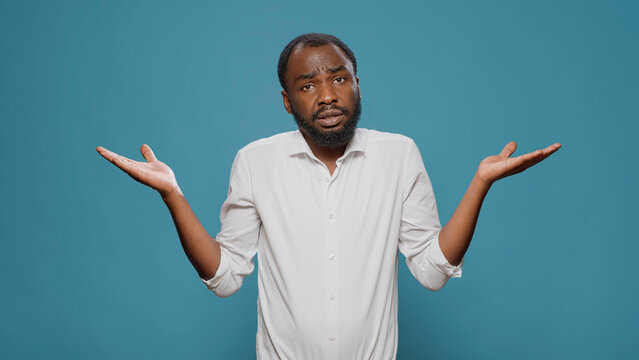 Uncertain clueless person doing i dont know gesture on camera, feeling doubtful and confused. Unsure man misunderstanding idea, feeling puzzled about unknown answer to question.
