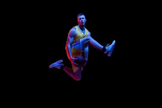 Portrait of sportive man, professional basketball player playing basketball isolated on dark background in neon light. Achievements, sport career, motion concepts.