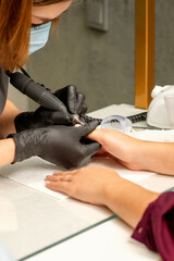 Fototapeta premium Manicure master wearing protective mask uses electric nail file machine in a nail salon, close up