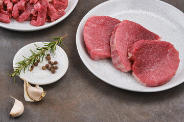 Fresh cut of beef in white plate with salt, pepper, garlic, rosemary. Raw steak beef meat fillet ready to cook. Selective focus