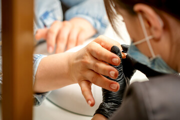 Manicure painting process. Manicure master paint the nails with transparent varnish in a nail salon, close up