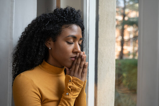 One black woman depressed in front of window prays