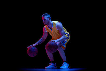 Dribbling. One sportive man, professional basketball player playing basketball isolated on dark background in neon light. Achievements, sport career, motion concepts.