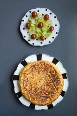 Two dishes, one Spanish omelette, and one green salad with roman lettuce, and cherry tomatoes with a grey background