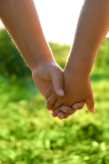 Two children holding hands, green natural blurred background. friends handshake close up. sunny summer's day. symbol of friendship, love, unity