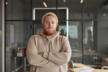 Portrait of young Caucasian app developer with beard standing with thermos mug and tablet in office