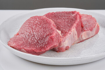 Fresh cut of beef in a white plate. Raw steak beef meat fillet ready to cook. Selective focus