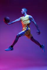 Fototapeta na wymiar Studio shot of muscled man, basketball player training with ball isolated on purple background in neon light. Goals, sport, motion, activity concepts.