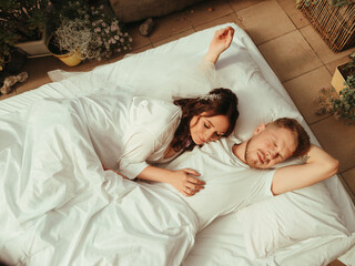 loving married couple lie on bed in hotel, relax together. man and woman in bathrobes have rest, leisure time, enjoy. grain effect