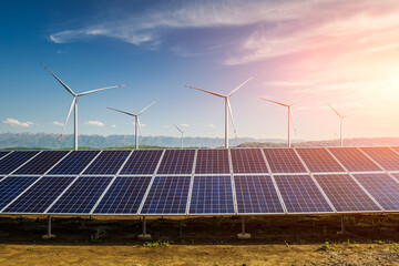 Solar panels and wind turbines with mountain landscape at sunset. Green energy concept.