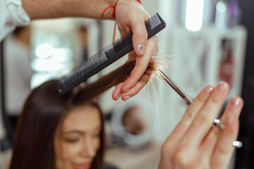 Close up of beautician hands holding a hair strand while cutting hair of woman. Hairstyling, beauty