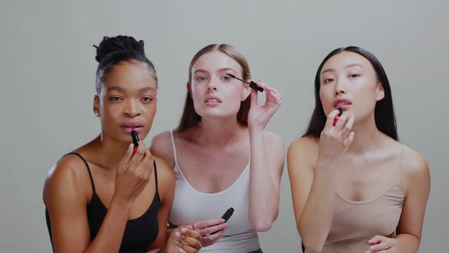 Trio of beautiful diverse women applying nude makeup cosmetic products using lipstick and mascara. Beauty procedure. Makeup concept. Isolated.