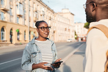 African-American girl in eyeglasses holding phone and asking stranger about route in big city