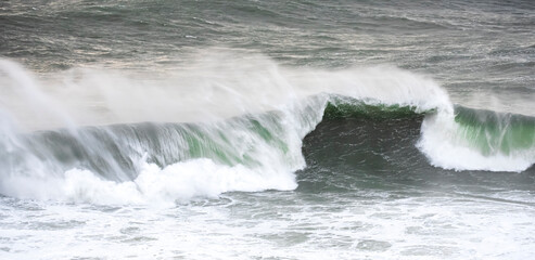 Big waves crashing on the sea with greenish blue color during a cloudy day