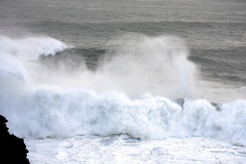 Big waves crashing on the sea with greenish blue color during a cloudy day