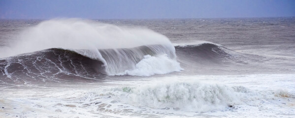 Big waves crashing on the sea with greenish blue color during a cloudy day